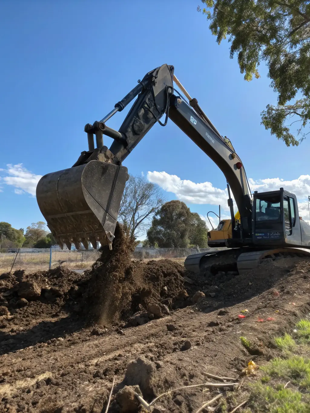 An excavator leveling and excavating a residential lot, with cleared land in the background, highlighting Hendersons Construction LLC's lot clearing and excavation services.